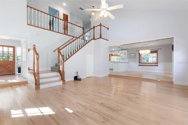 unfurnished living room featuring a high ceiling, light wood-type flooring, and ceiling fan with notable chandelier