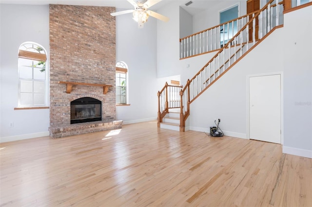 unfurnished living room with ceiling fan, brick wall, a brick fireplace, light wood-type flooring, and a towering ceiling