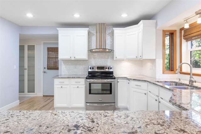 kitchen with white cabinets, stainless steel range with electric stovetop, sink, and wall chimney range hood