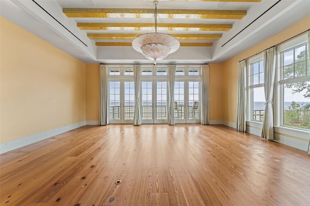 empty room featuring beamed ceiling, a healthy amount of sunlight, a tray ceiling, and light hardwood / wood-style floors