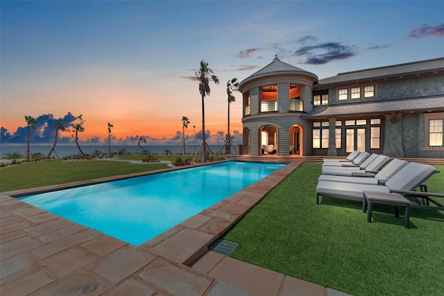 pool at dusk with a lawn and a patio