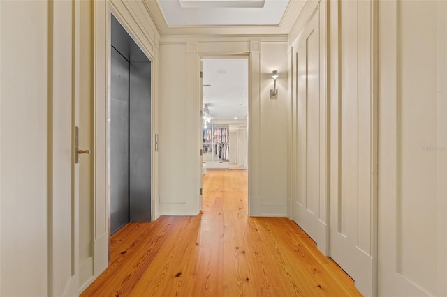 hallway featuring crown molding, elevator, and light wood-type flooring