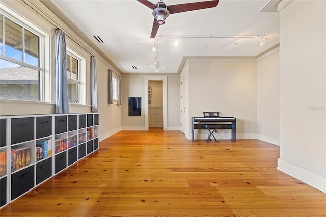 empty room featuring track lighting, crown molding, ceiling fan, and light hardwood / wood-style flooring