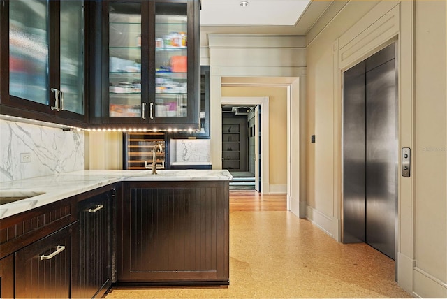 bar with dark brown cabinets, backsplash, elevator, light stone countertops, and crown molding