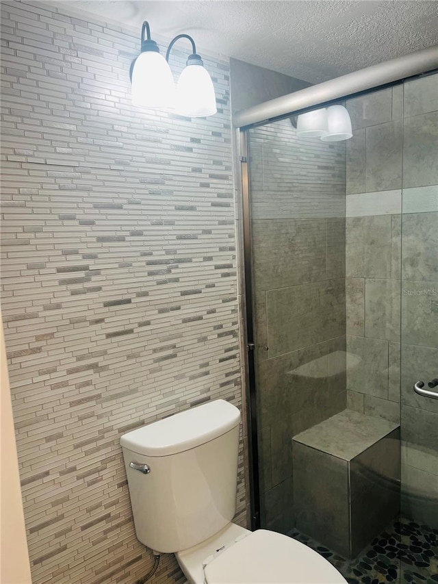 bathroom with a textured ceiling, a shower with shower door, toilet, and tile walls