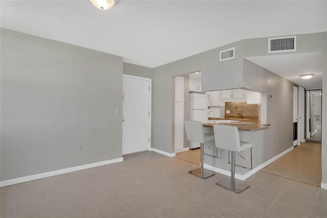 kitchen with white cabinetry, a kitchen breakfast bar, kitchen peninsula, white fridge, and decorative backsplash