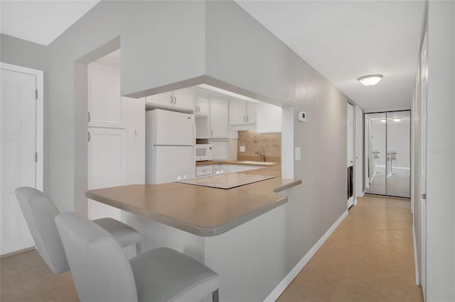 kitchen featuring white cabinets, white appliances, kitchen peninsula, and a breakfast bar area