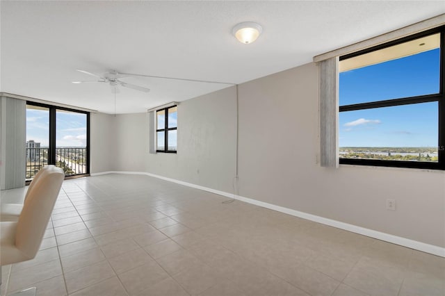 tiled spare room featuring ceiling fan and floor to ceiling windows