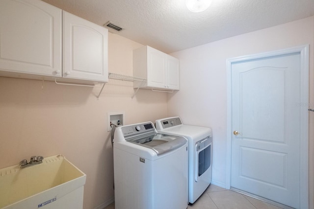 laundry room with cabinets, separate washer and dryer, a textured ceiling, sink, and light tile patterned flooring