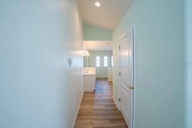 corridor with light hardwood / wood-style flooring and vaulted ceiling