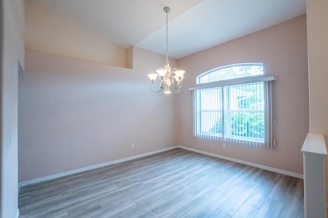 spare room with hardwood / wood-style flooring, lofted ceiling, plenty of natural light, and an inviting chandelier