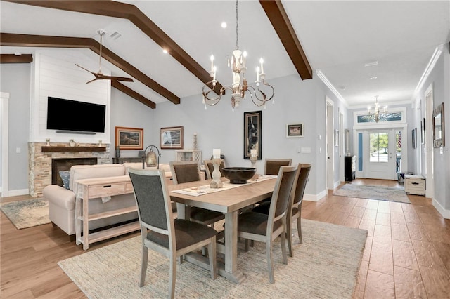 dining space with light wood-type flooring, french doors, a stone fireplace, and high vaulted ceiling