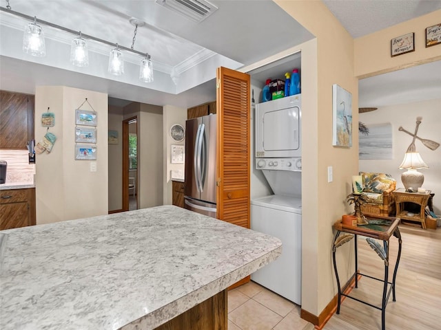 kitchen with stacked washer and dryer, crown molding, stainless steel fridge, and light tile flooring