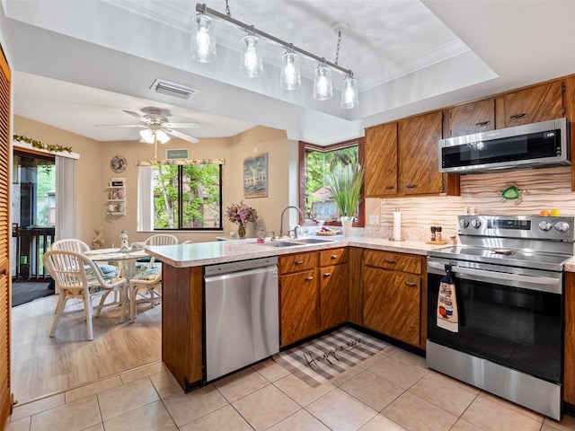 kitchen featuring a tray ceiling, kitchen peninsula, light tile floors, and appliances with stainless steel finishes