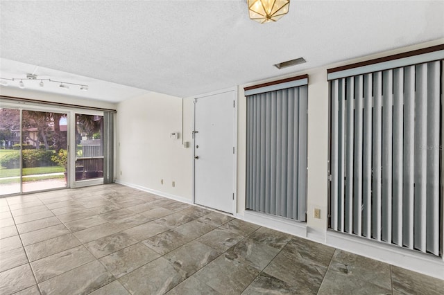 empty room with a textured ceiling, track lighting, and tile flooring