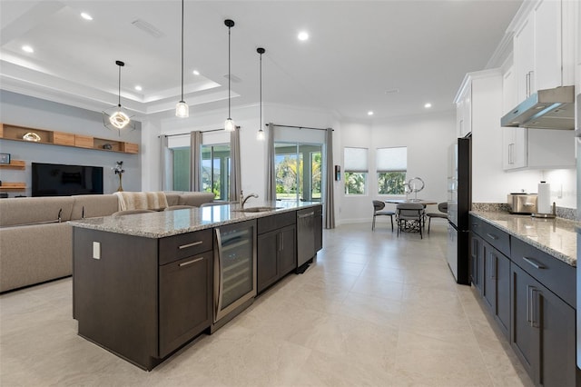 kitchen featuring decorative light fixtures, light stone countertops, wine cooler, a center island with sink, and white cabinets