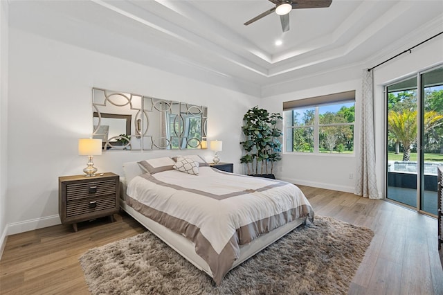 bedroom featuring ceiling fan, access to exterior, light wood-type flooring, and a tray ceiling