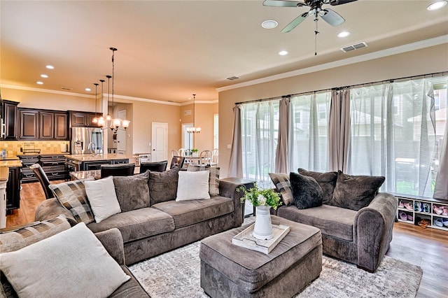 living room with plenty of natural light, ornamental molding, light hardwood / wood-style flooring, and ceiling fan with notable chandelier