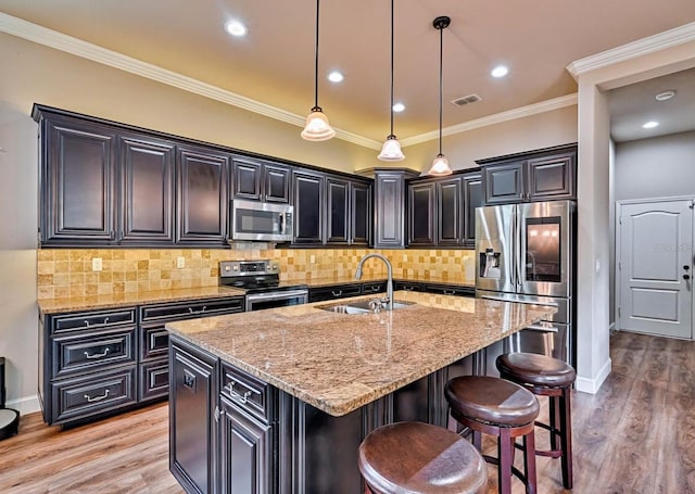 kitchen featuring a center island with sink, appliances with stainless steel finishes, pendant lighting, and light wood-type flooring