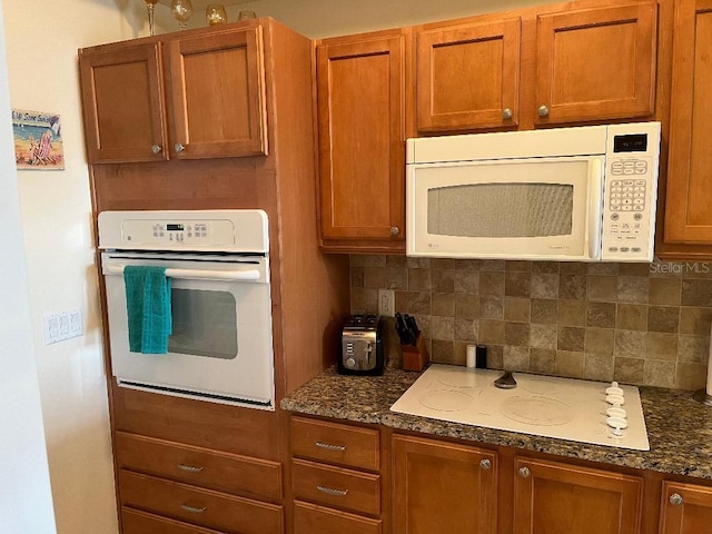 kitchen with dark stone counters, white appliances, and decorative backsplash