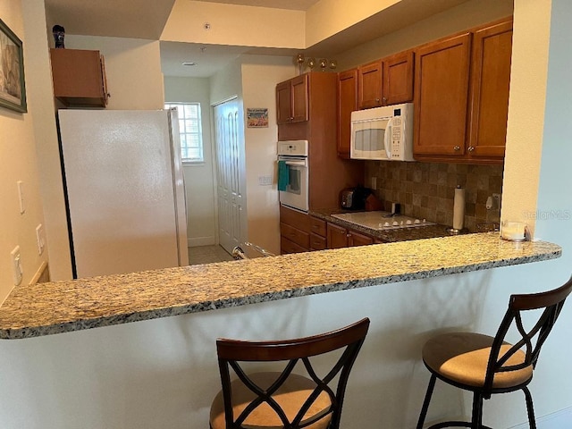 kitchen with white appliances, a kitchen bar, kitchen peninsula, and light stone countertops