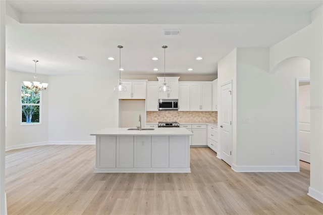 kitchen with an island with sink, sink, light hardwood / wood-style flooring, white cabinetry, and appliances with stainless steel finishes