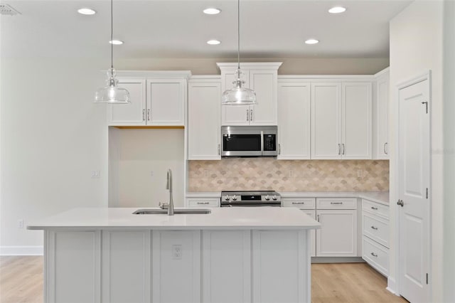 kitchen featuring hanging light fixtures, a center island with sink, stainless steel appliances, and white cabinets