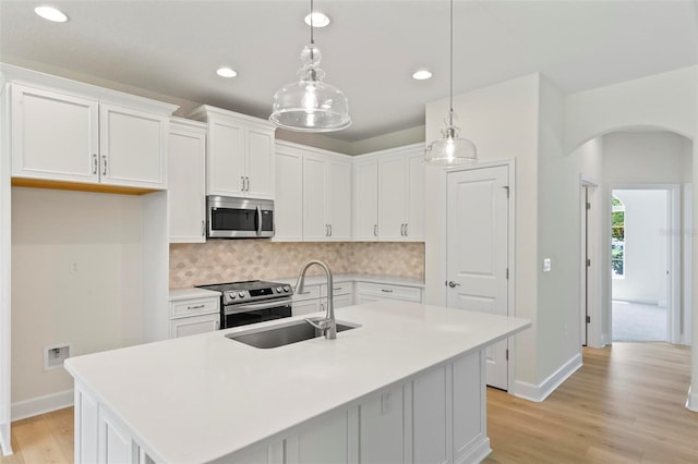 kitchen with white cabinets, a center island with sink, decorative light fixtures, appliances with stainless steel finishes, and light hardwood / wood-style floors