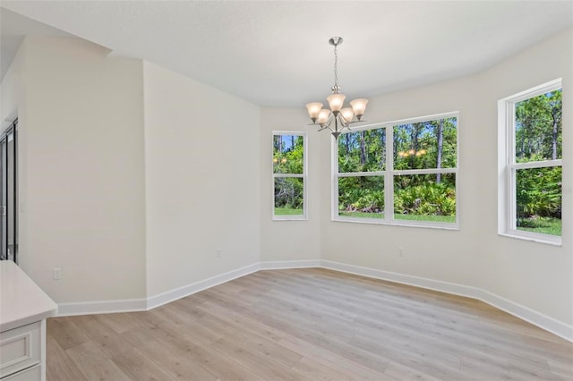 spare room featuring a chandelier, light hardwood / wood-style floors, and a healthy amount of sunlight