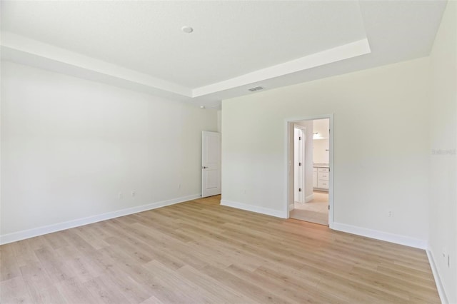 spare room featuring a tray ceiling and light hardwood / wood-style flooring