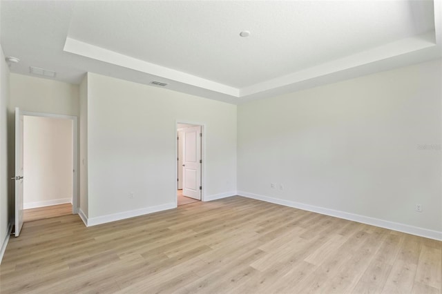 unfurnished room featuring light wood-type flooring and a tray ceiling