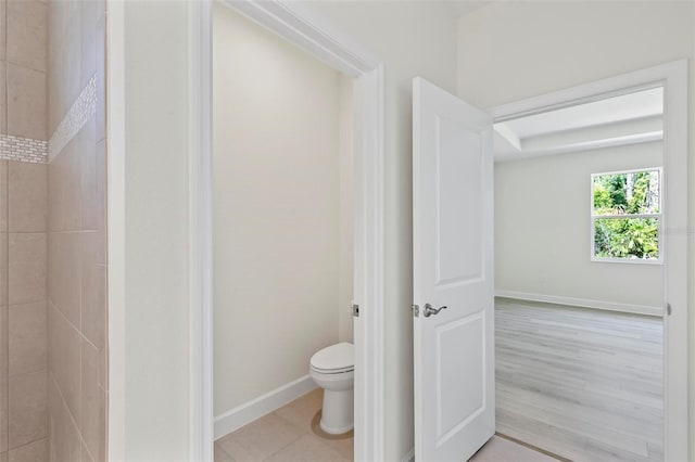 bathroom featuring wood-type flooring, toilet, and tiled shower