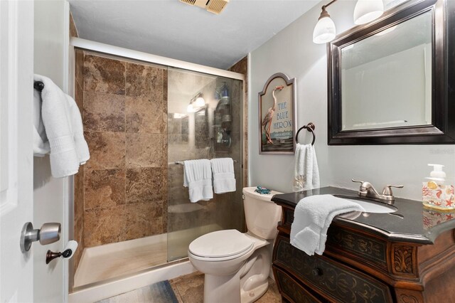 bathroom featuring tile floors, toilet, vanity, and a shower with door