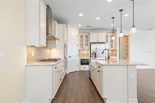 kitchen featuring tasteful backsplash, wall chimney range hood, pendant lighting, sink, and a kitchen island with sink