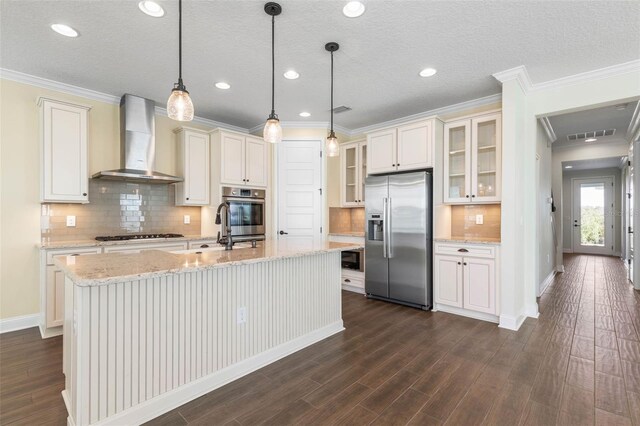 kitchen featuring stainless steel fridge with ice dispenser, tasteful backsplash, a kitchen island with sink, pendant lighting, and wall chimney exhaust hood