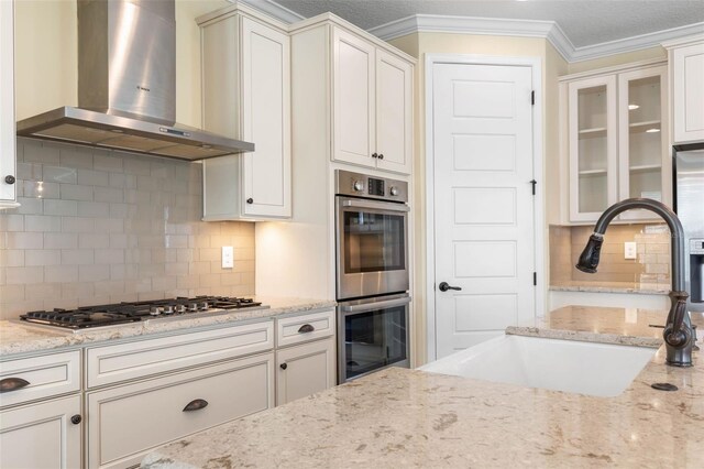 kitchen with backsplash, wall chimney range hood, sink, appliances with stainless steel finishes, and light stone counters