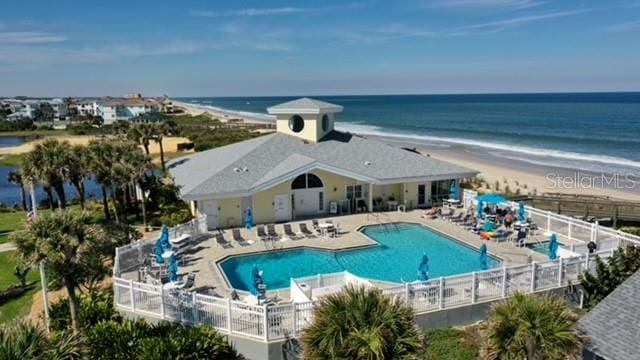 view of swimming pool with a water view, a view of the beach, and a patio area