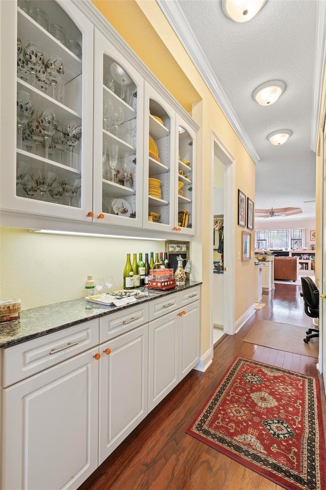 bar with ceiling fan, dark hardwood / wood-style flooring, dark stone countertops, a textured ceiling, and white cabinets