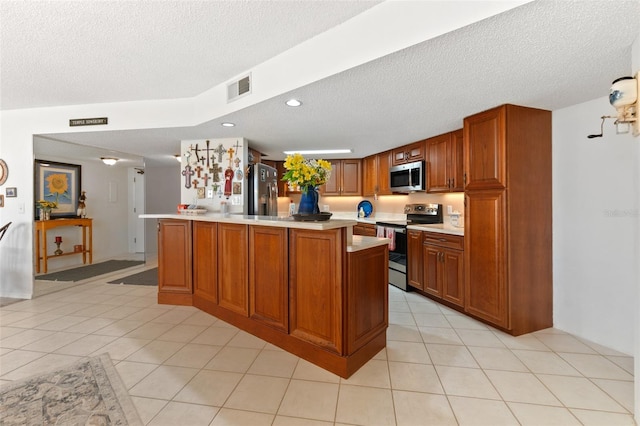 kitchen featuring a textured ceiling, a kitchen island with sink, light tile floors, and appliances with stainless steel finishes