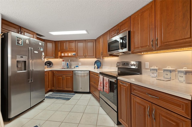 kitchen with a textured ceiling, appliances with stainless steel finishes, light tile floors, and sink