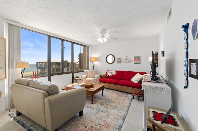 living room with light tile flooring, a wall of windows, ceiling fan, and a textured ceiling