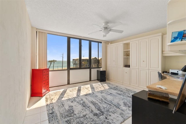 interior space with ceiling fan, a textured ceiling, a water view, and light tile floors