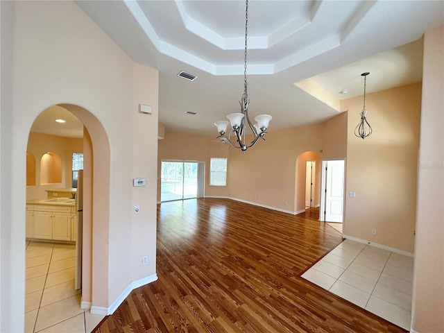 tiled empty room featuring sink, a raised ceiling, and a chandelier