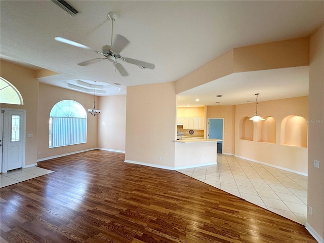 tiled empty room featuring ceiling fan with notable chandelier and a raised ceiling