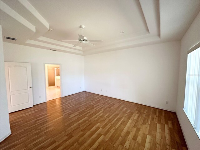 spare room with ceiling fan, dark hardwood / wood-style floors, a tray ceiling, and a wealth of natural light