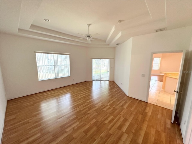 empty room with a raised ceiling, ceiling fan, and light hardwood / wood-style flooring