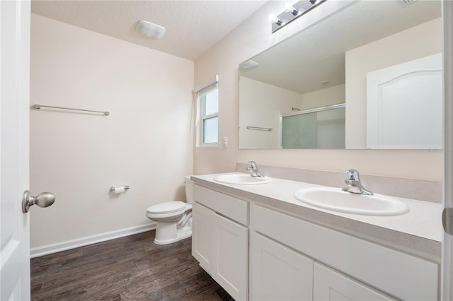 bathroom with toilet, vanity with extensive cabinet space, wood-type flooring, dual sinks, and a textured ceiling