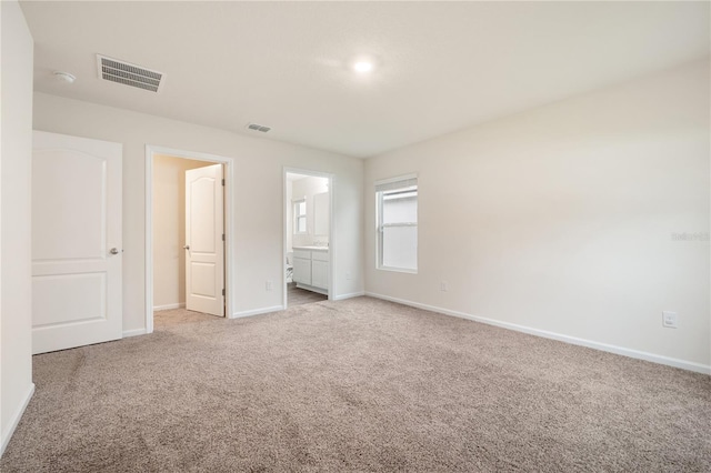 unfurnished bedroom featuring light carpet and ensuite bath