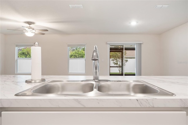 kitchen with ceiling fan, sink, and light stone counters