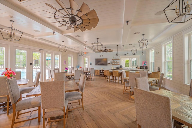 dining space with light parquet flooring, a healthy amount of sunlight, ceiling fan with notable chandelier, and beamed ceiling